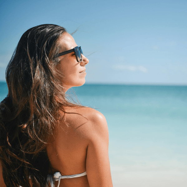 Blobbeitrags_Teaserbild: "EMS-Training im Sommer". Frau mit Sonnenbrille schaut zufrieden zur Seite. Im Hintergrund ist ein klarer Strand zu erkennen.